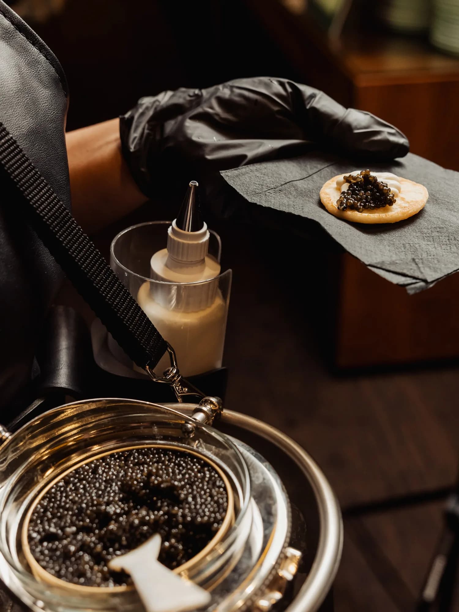 A gloved server assembling a caviar blini beside an open tin